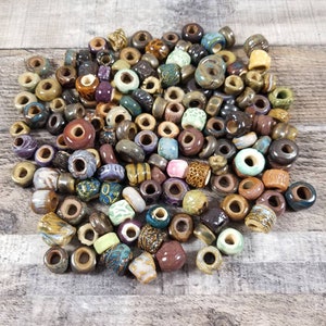 May include: A large pile of colorful ceramic beads with various patterns and textures. The beads are a mix of brown, green, blue, purple, and pink.