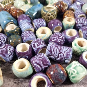 May include: A collection of colorful ceramic beads with various patterns and designs. The beads are a mix of purple, green, brown, and blue.