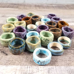 May include: A collection of ceramic rings in various shades of blue, green, brown, and purple. The rings are stacked and arranged in a circular pattern.