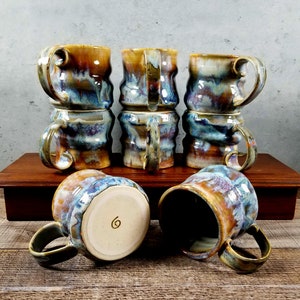 May include: Six ceramic mugs with a blue, brown, and yellow glaze. The mugs are stacked in pairs and have a unique, wavy design.