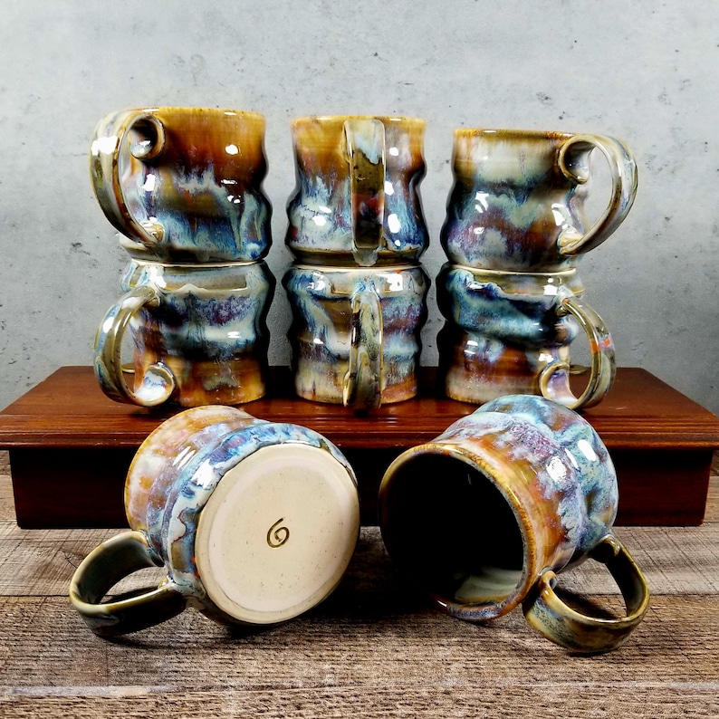 May include: Six ceramic mugs with a blue, brown, and yellow glaze. The mugs are stacked in pairs and have a unique, wavy design.
