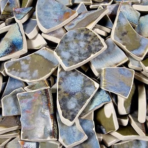 May include: A pile of ceramic tile pieces in various shades of blue, green, and brown. The tiles are irregular in shape and have a textured surface.