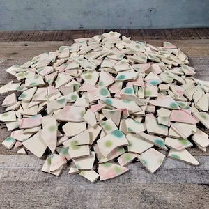 May include: A pile of white ceramic tile pieces with pink and green speckled glaze. The tiles are broken into various shapes and sizes.
