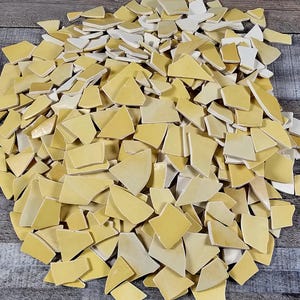 May include: A large pile of yellow ceramic tile pieces, some with a white glaze, perfect for mosaic projects.