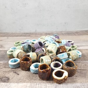 Pu&ograve; includere: Un mucchio di anelli in ceramica colorati, alcuni con una superficie testurizzata, in tonalit&agrave; di verde, blu, marrone e viola.