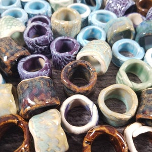 Pu&ograve; includere: Una collezione di anelli in ceramica di vari colori e motivi, tra cui blu, verde, viola, marrone e bianco. Gli anelli sono di diverse dimensioni e forme, e alcuni hanno una superficie testurizzata.