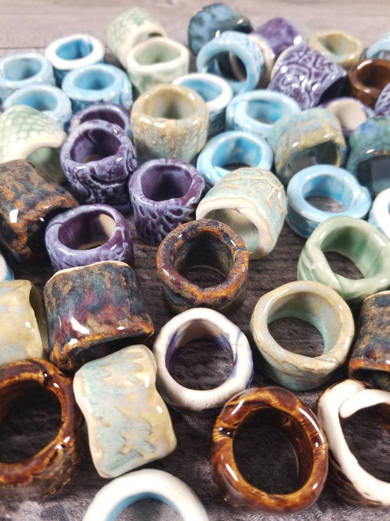 Pu&ograve; includere: Una collezione di anelli in ceramica di vari colori e motivi, tra cui blu, verde, viola, marrone e bianco. Gli anelli sono di diverse dimensioni e forme, e alcuni hanno una superficie testurizzata.