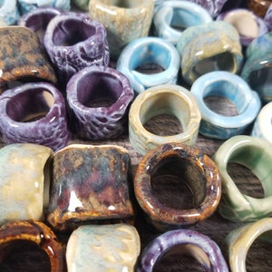 Pu&ograve; includere: Una collezione di anelli in ceramica di vari colori e motivi, tra cui blu, viola, marrone e verde. Gli anelli sono smaltati e hanno una finitura liscia e lucida.