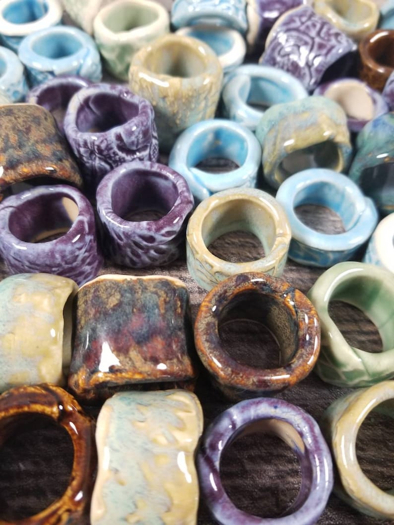 Pu&ograve; includere: Una collezione di anelli in ceramica di vari colori e motivi, tra cui blu, viola, marrone e verde. Gli anelli sono smaltati e hanno una finitura liscia e lucida.