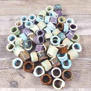 Pu&ograve; includere: Una collezione di anelli in ceramica di vari colori e motivi, tra cui blu, verde, marrone e viola. Gli anelli sono impilati e sparsi su una superficie di legno.
