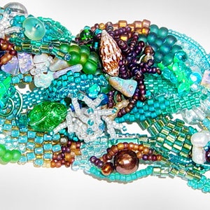 Pode incluir: Um bracelete de contas com uma mistura de contas turquesa, verdes, marrons e brancas. O bracelete é feito com uma variedade de formas e tamanhos de contas, criando um visual único e texturizado.