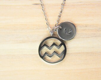 May include: Silver necklace with a round pendant featuring a cut-out Aquarius zodiac sign and a smaller round pendant with the letter 'C'.