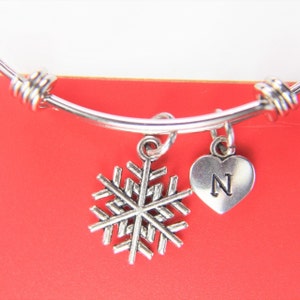 May include: A silver expandable bangle bracelet with a snowflake charm and a heart charm with the letter "N" engraved on it.