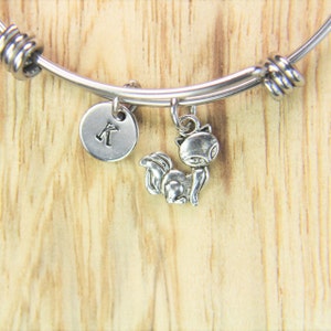 May include: A silver charm bracelet with a silver charm of a fox and a silver charm with the letter K.