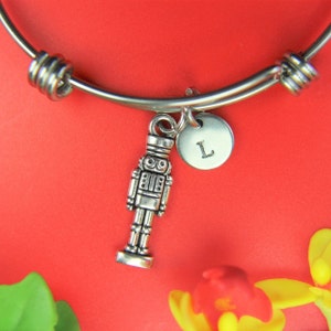 May include: A silver charm bracelet with a nutcracker charm and a silver disc charm with the letter "L" on it. The bracelet is on a red background.