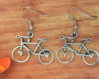 May include: A pair of silver bicycle earrings with heart details. The earrings are hanging from silver hooks.