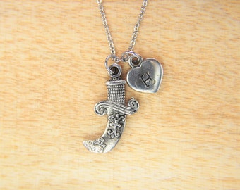 May include: Silver necklace with a silver dagger charm and a silver heart charm with the letter H engraved on it.