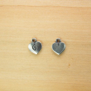 May include: Two silver heart-shaped charms, one with the letter "G" engraved on it.
