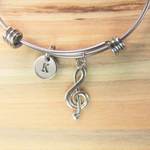 May include: A silver charm bracelet with a treble clef charm and a round charm with the letter K engraved on it.
