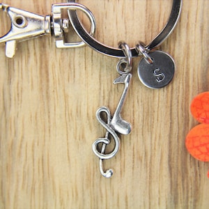 May include: Silver key chain with a treble clef charm and a small round charm with the letter 'S' on it.