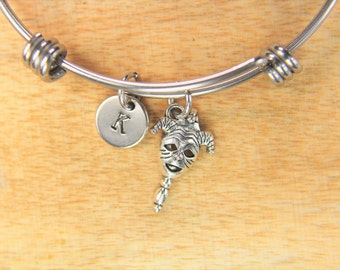 May include: A silver charm bracelet with a jester charm and a personalized initial charm. The bracelet is made of stainless steel and has a simple design.