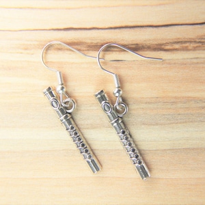 May include: A pair of silver earrings shaped like flutes. The flutes have a detailed design with small circles.