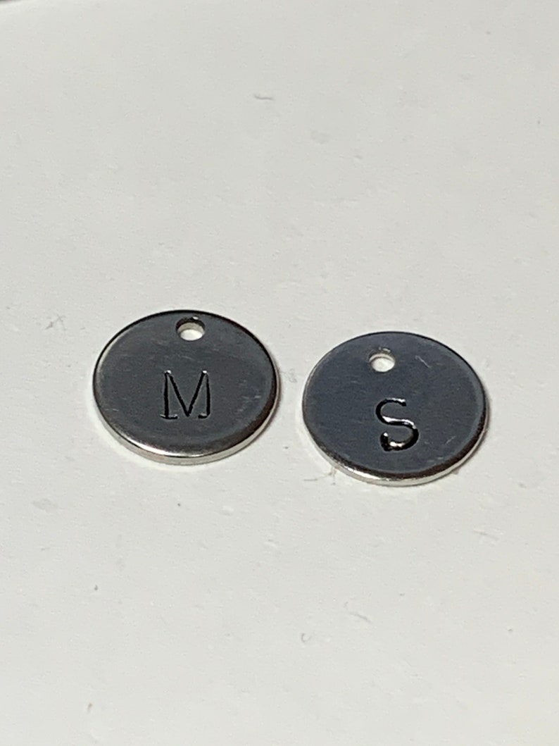 May include: Two silver metal round charms with the letters M and S engraved on them.