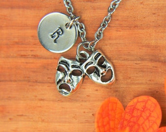 May include: A silver necklace with a round charm that says "R" and two silver charms shaped like theater masks. One mask is smiling and the other is frowning.