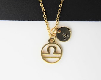 May include: Gold necklace with a Libra zodiac symbol charm and a small charm with the letter A.
