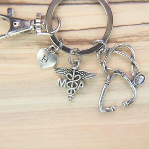 May include: Silver keychain with a medical symbol charm, a stethoscope charm, and a heart charm with the letter H engraved on it.