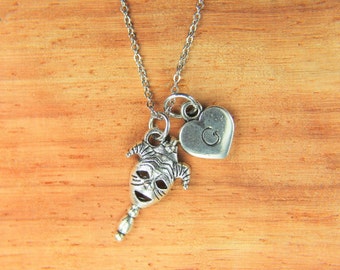 May include: A silver necklace with a heart charm and a jester mask charm. The heart charm has the letter "G" engraved on it.