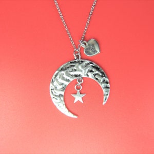 May include: A silver necklace with a crescent moon pendant and a dangling star charm. The necklace also features a small heart charm with the letter 'S' engraved on it.