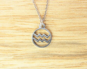 May include: A silver necklace with a round pendant featuring a wavy design. The pendant is hanging on a silver chain.