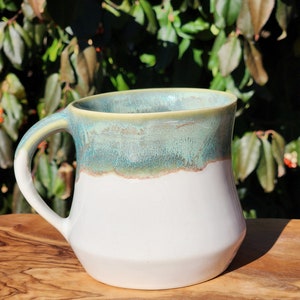 May include: A white ceramic mug with a teal and green glaze. The mug has a wide base and a rounded handle.