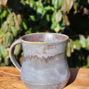 May include: A ceramic mug with a light blue glaze and a brown rim. The mug has a wide base and a handle.