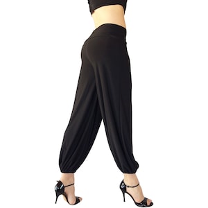 May include: Black, loose-fitting trousers with a gathered elastic waistband. The trousers are made of a soft, stretchy fabric and have a wide leg.