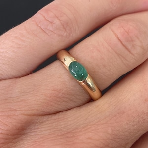 May include: A gold ring with a vibrant green gemstone. The gemstone is oval-shaped and set in a polished gold band. The ring's design is simple yet elegant, showcasing the gemstone's color and brilliance.