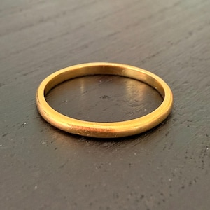 Peut inclure: Une bague dorée avec un anneau lisse et arrondi. La bague est posée sur un fond sombre, ce qui met en valeur son éclat métallique. Le design simple de la bague suggère qu'il pourrait s'agir d'une alliance ou d'un accessoire de mode minimaliste.