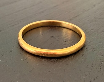 May include: A gold-colored ring with a smooth, rounded band. The ring is set against a dark background, highlighting its metallic sheen. The ring's simple design suggests it could be a wedding band or a minimalist fashion accessory.