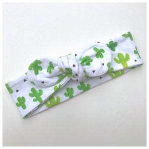 May include: White headband with a green cactus print and black triangle accents. The headband is tied in a knot at the top.