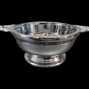 May include: A silver serving bowl with two decorative handles. The bowl features an ornate band around the middle and a pedestal base. The interior of the bowl is highly reflective.