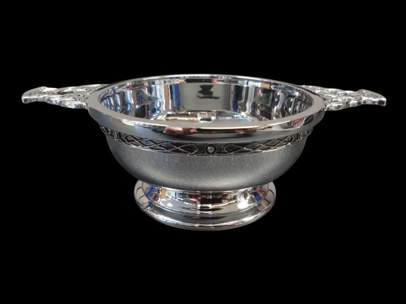 May include: A silver serving bowl with two decorative handles. The bowl features an ornate band around the middle and a pedestal base. The interior of the bowl is highly reflective.