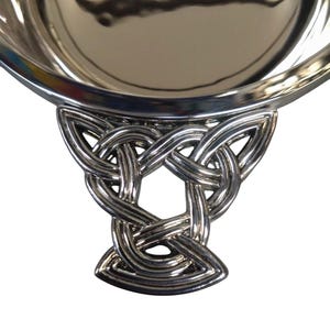 May include: A silver serving bowl with a Celtic knot handle. The bowl has a reflective surface, and the handle features an intricate, interwoven pattern. The bowl is likely made of metal. The bowl's diameter is approximately 20 cm.