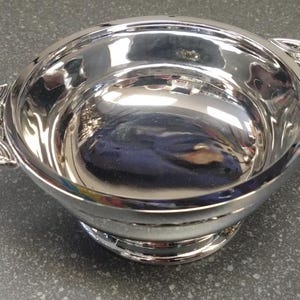 May include: A polished silver bowl with Celtic knot handles. The bowl is round with a small base and reflects the surroundings. The handles are intricately designed with a Celtic knot pattern.