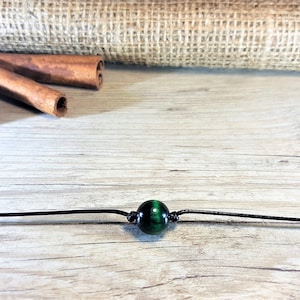 Könnte beinhalten: Eine einfache schwarze Schnurkette mit einer einzigen grünen Tigerauge-Perle.