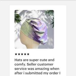 May include: A slouchy beanie hat featuring a tie-dye pattern in shades of pastel purple, soft green, and white. The hat has a wide, fitted band at the base and gathered fabric at the crown, creating a relaxed, voluminous silhouette on a mannequin head.