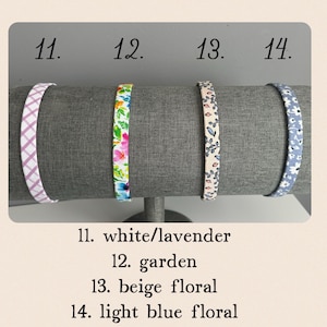 Puede incluir: Cuatro diademas de tela expuestas en un soporte. Las diademas son de diferentes patrones: a cuadros blancos y lavanda, florales con acentos rosas y verdes, florales beige y florales azul claro. Los n&uacute;meros 11, 12, 13 y 14 est&aacute;n escritos encima de cada diadema.