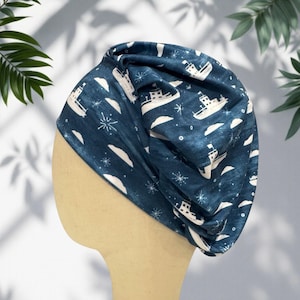 May include: A dark blue slouchy beanie hat featuring a repeating pattern of white boats, clouds, and starburst shapes. The fabric has a soft, gathered texture, creating a relaxed fit that sits comfortably on the head with a rounded silhouette.