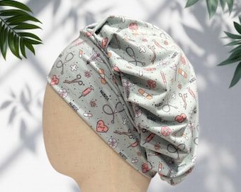 May include: A light green scrub cap featuring a repeating pattern of medical icons including stethoscopes, syringes, bandages, hearts, and the word nurse in black text. The fabric is gathered at the top and sides, creating a soft, pleated appearance.