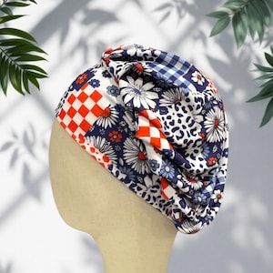 May include: A fabric head wrap featuring a patchwork design of white daisies on a navy blue background, red and white checkered squares, blue and white gingham, and a black and white animal print pattern with gathered folds and a soft texture.